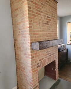 brown custom wood mantel being installed on a brick fireplace